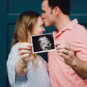 man kissing woman's forehead white holding ultrasound photo