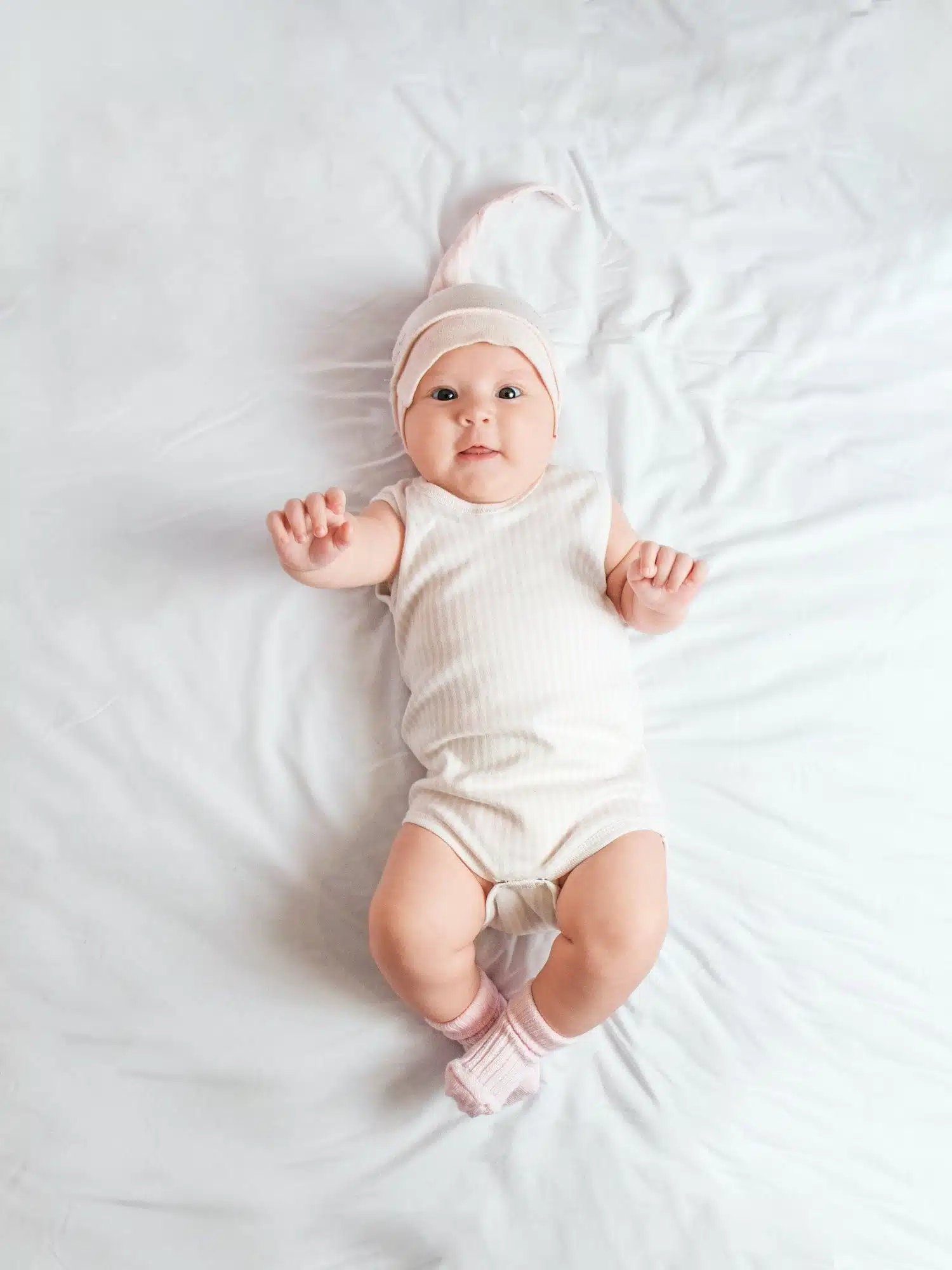 cute baby in a pink hat lies on the bed, top view